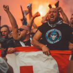 Njaveći derbiji Bakana. Fudbal. Navijači. Fudbalski navijači pjevaju dok idu na utakmicu držeći zastavu i upaljene baklje.