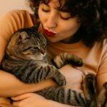 Hug your cat day, mačke, mačke i ljudi, Žena sa crvenim ružem nježno grli svoju tigrastu mačku u toplom ambijentu