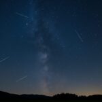 Astronomski događaji 2025, Noćno nebo sa kišom meteora tokom Perzeida iznad mirnog pejzaža, uz vidljivu Mliječnu stazu i siluete drveća.