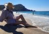 kreme za sunčanje, Žena na plaži sa šeširom u hladu, simbolizuje ljetnu zaštitu od sunca