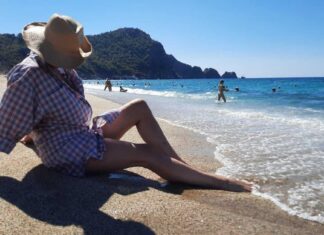 kreme za sunčanje, Žena na plaži sa šeširom u hladu, simbolizuje ljetnu zaštitu od sunca