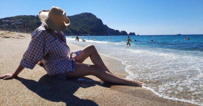 kreme za sunčanje, Žena na plaži sa šeširom u hladu, simbolizuje ljetnu zaštitu od sunca