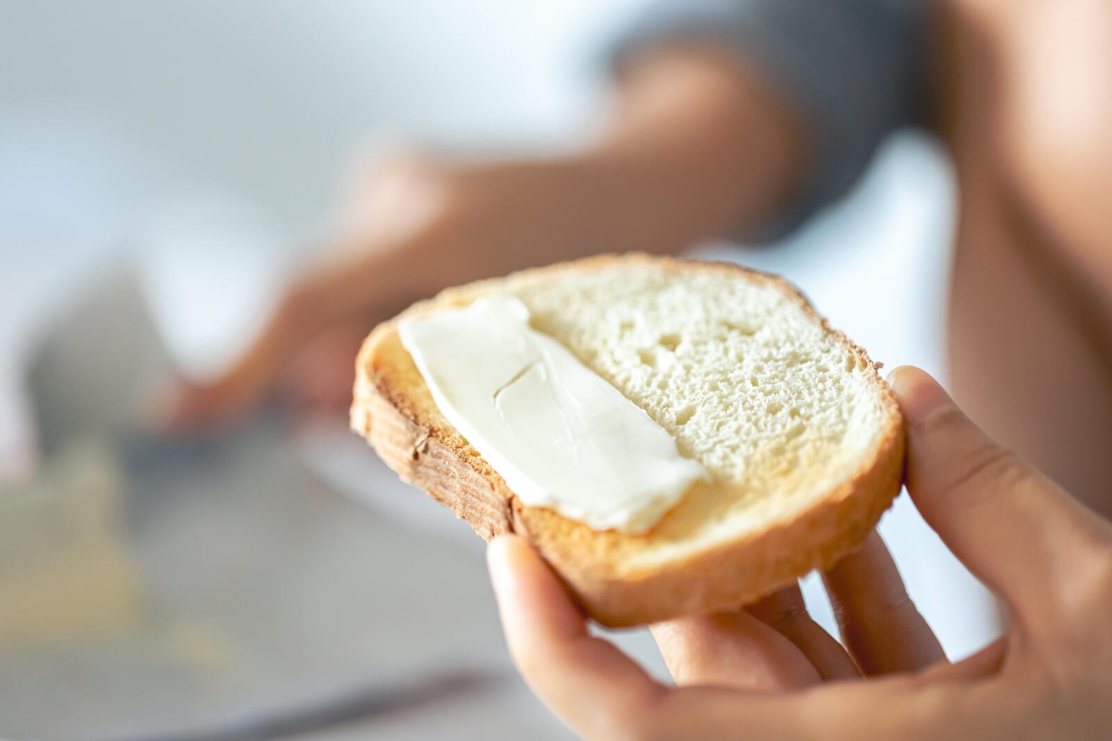 A piece of bread with butter in a woman's hand.