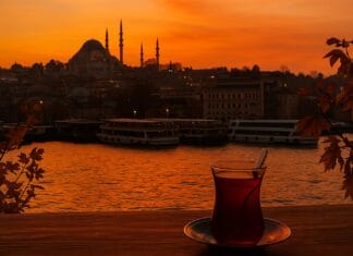 Istanbul grad kojem se vraćamo: U vagonu gdje tugujemo bez tuge Istanbul grad kojem se vraćamo, Čaša turskog čaja na drvenom stolu uz zalazak sunca nad Bosforom, s pogledom na istanbulske džamije u jesenjim bojama.