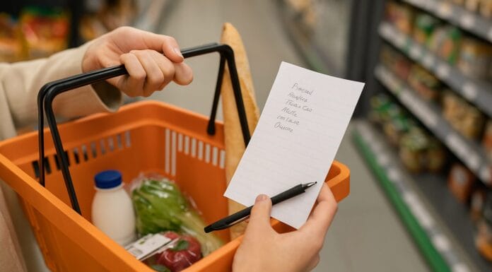 Međunarodni dan štednje – ruka drži papirni spisak za kupovinu pored korpe s osnovnim namirnicama poput hljeba, mlijeka i povrća; simbol planirane i racionalne potrošnje.
