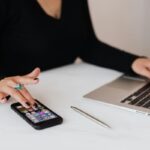 Žena koristi mobilni telefon dok radi na laptopu