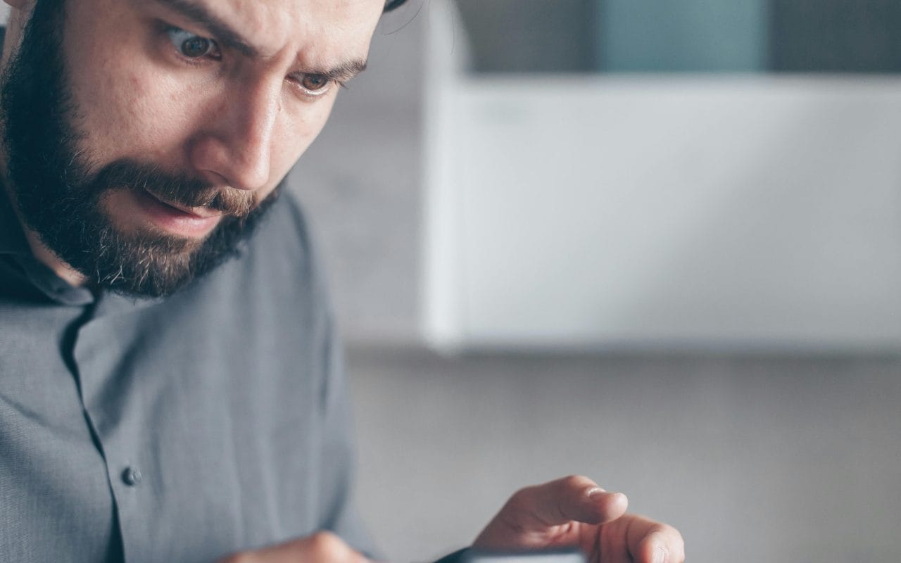 Čovek u sivoj košulji gleda u mobilni telefon