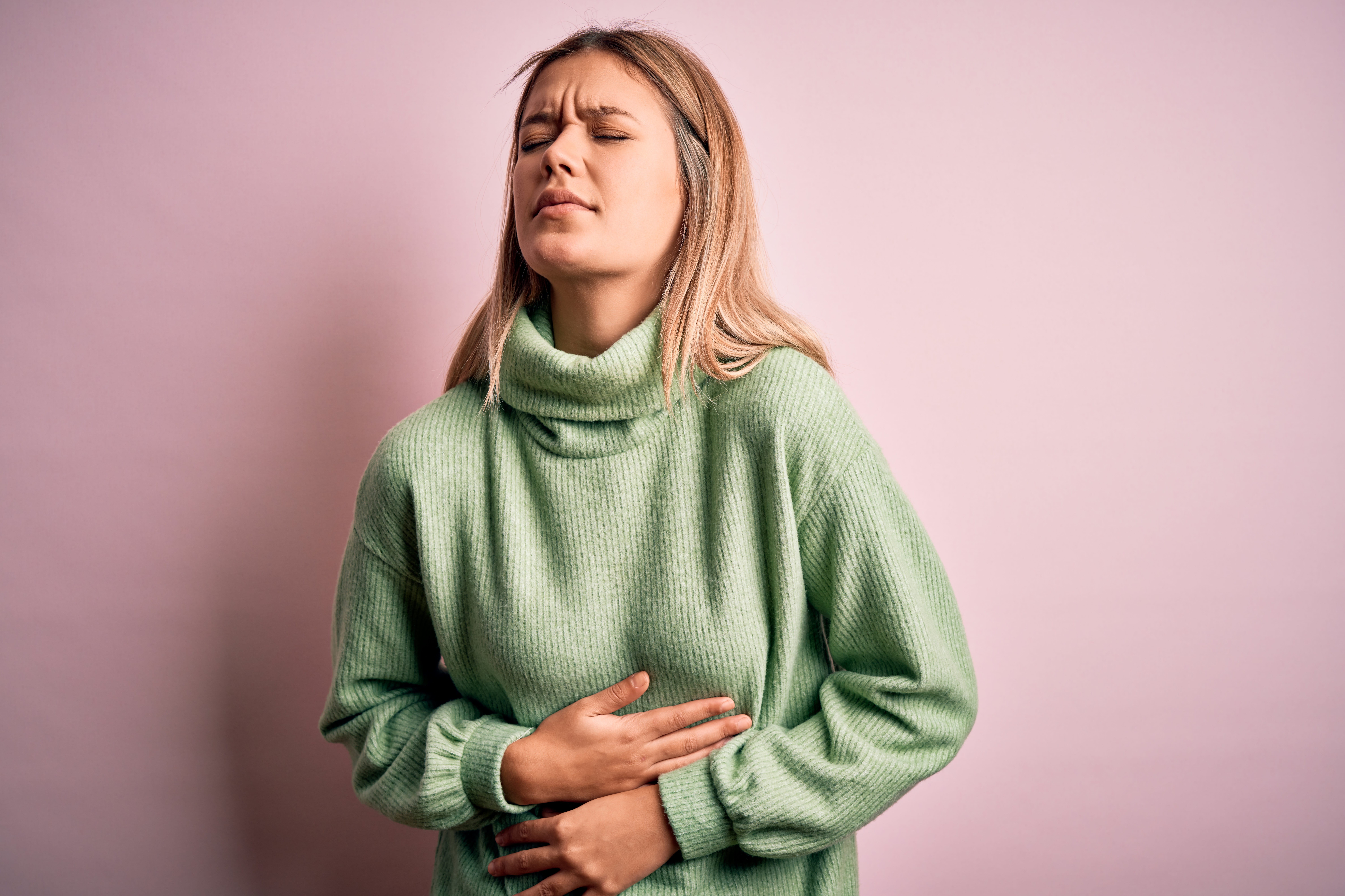 Young beautiful blonde woman wearing winter wool sweater over pink isolated background with hand on stomach because nausea, painful disease feeling unwell. Ache concept.