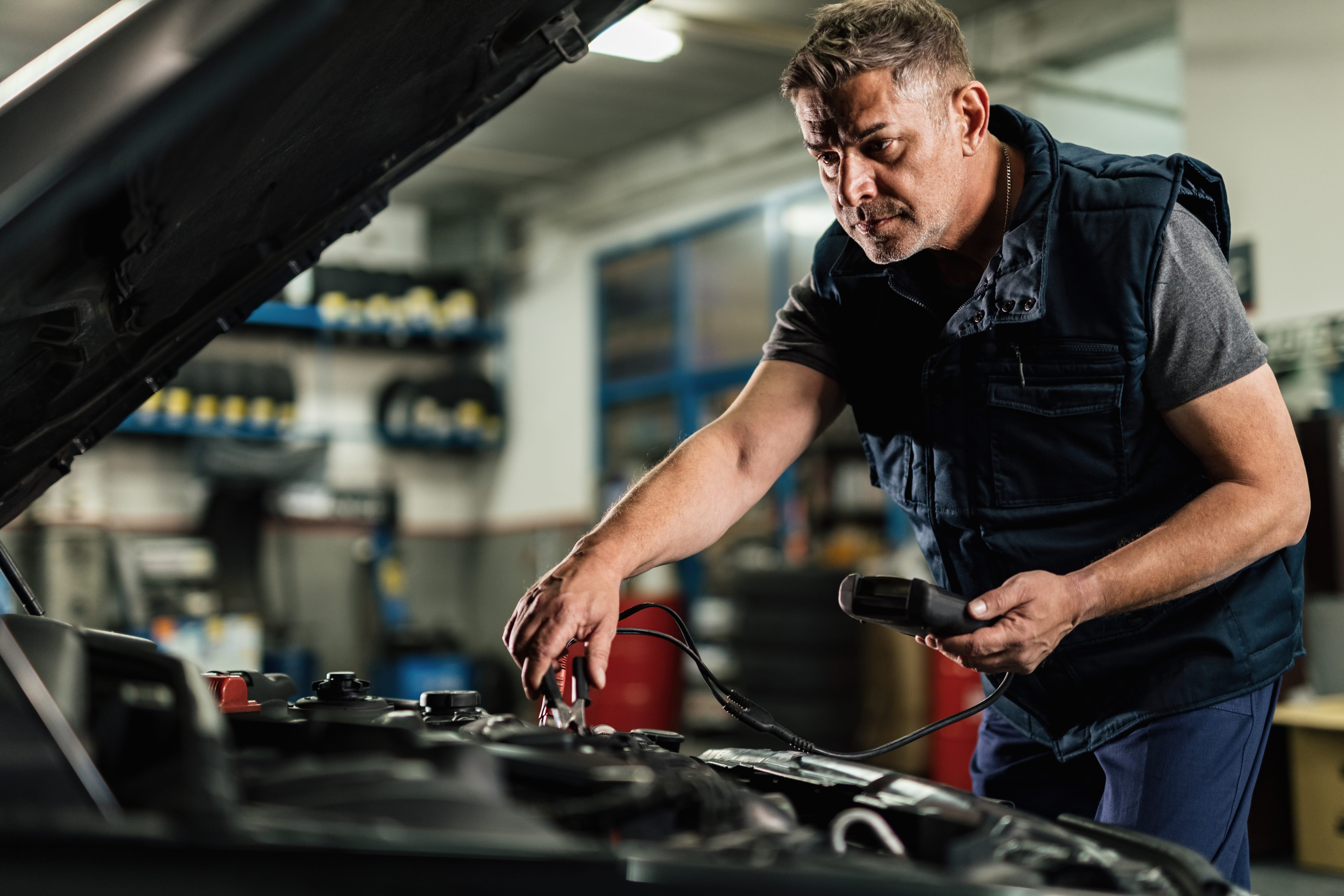 Auto mechanic repairing an engine and doing car battery check at