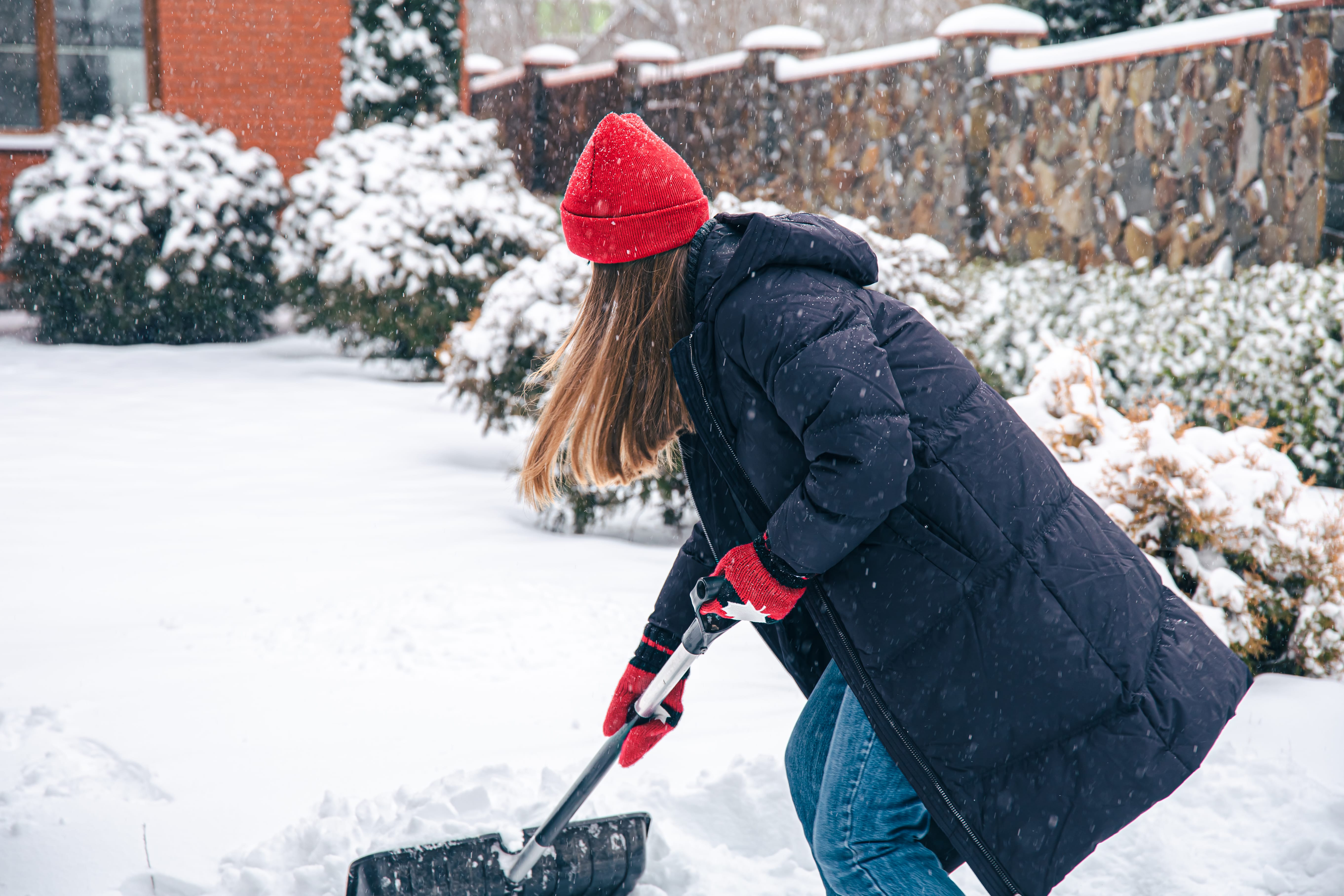 Young woman cleans snow in the yard in snowy weather.