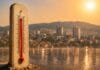 Toplotni val u Tuzli, termometar u prvom planu i gradska panorama u izmaglici od vrućine