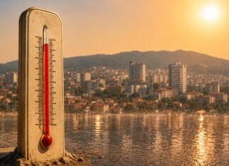 Toplotni val u Tuzli, termometar u prvom planu i gradska panorama u izmaglici od vrućine