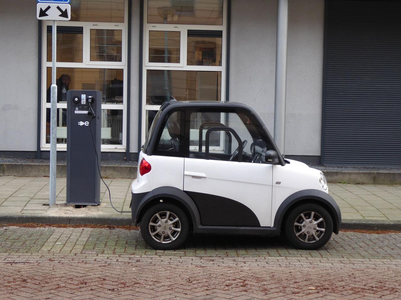 mali-beli-elektricni-automobil Mali beli električni automobil priključen na stanicu za punjenje