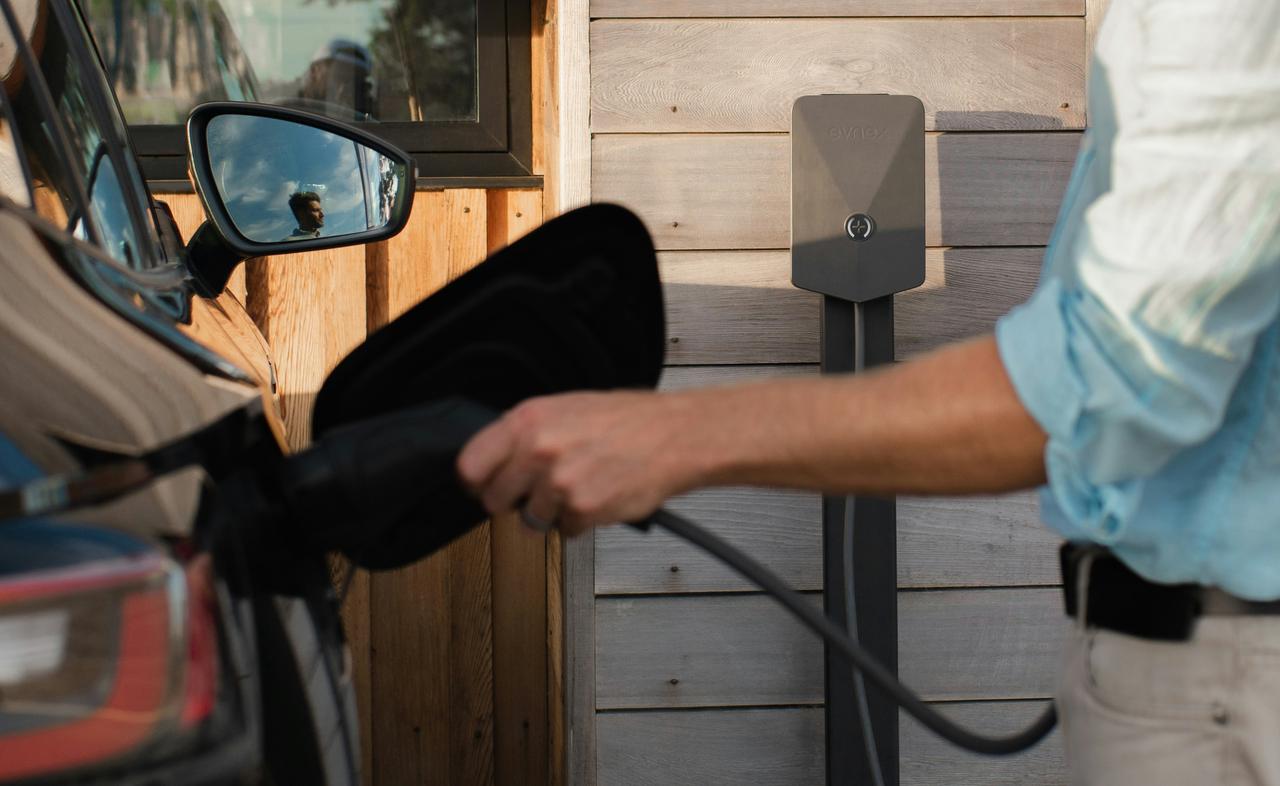 Osoba priključuje kabl punjača na električni automobil pored drvene obloge